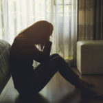 depressed woman sitting head in hands in the dark bedroom